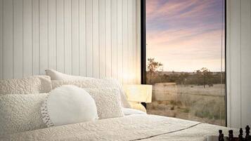 A bedroom with a large window, a bed with white bedding, and a lamp on the nightstand.