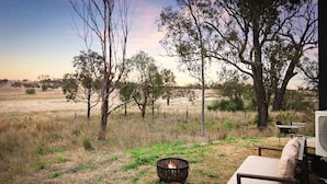 An outdoor seating area with a fire pit, a sofa, and a fan. - Charming Tiny House with Panoramic Views of the Valley in Queensland, Australia (Goombungee)