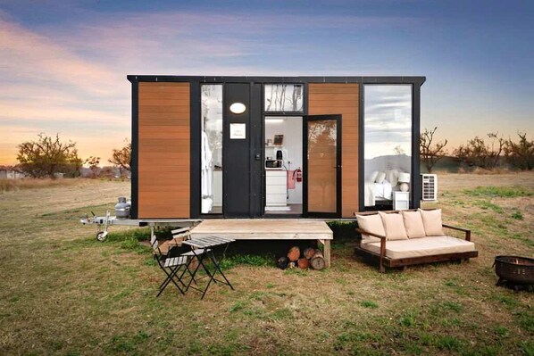 A modern mobile home with a kitchen, a sleeping area, and a small outdoor seating area.