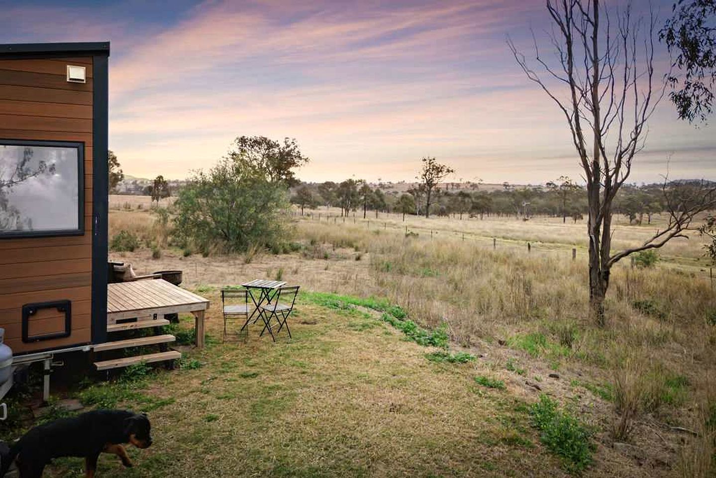 A wooden cabin with a deck, a table, and chairs outside.