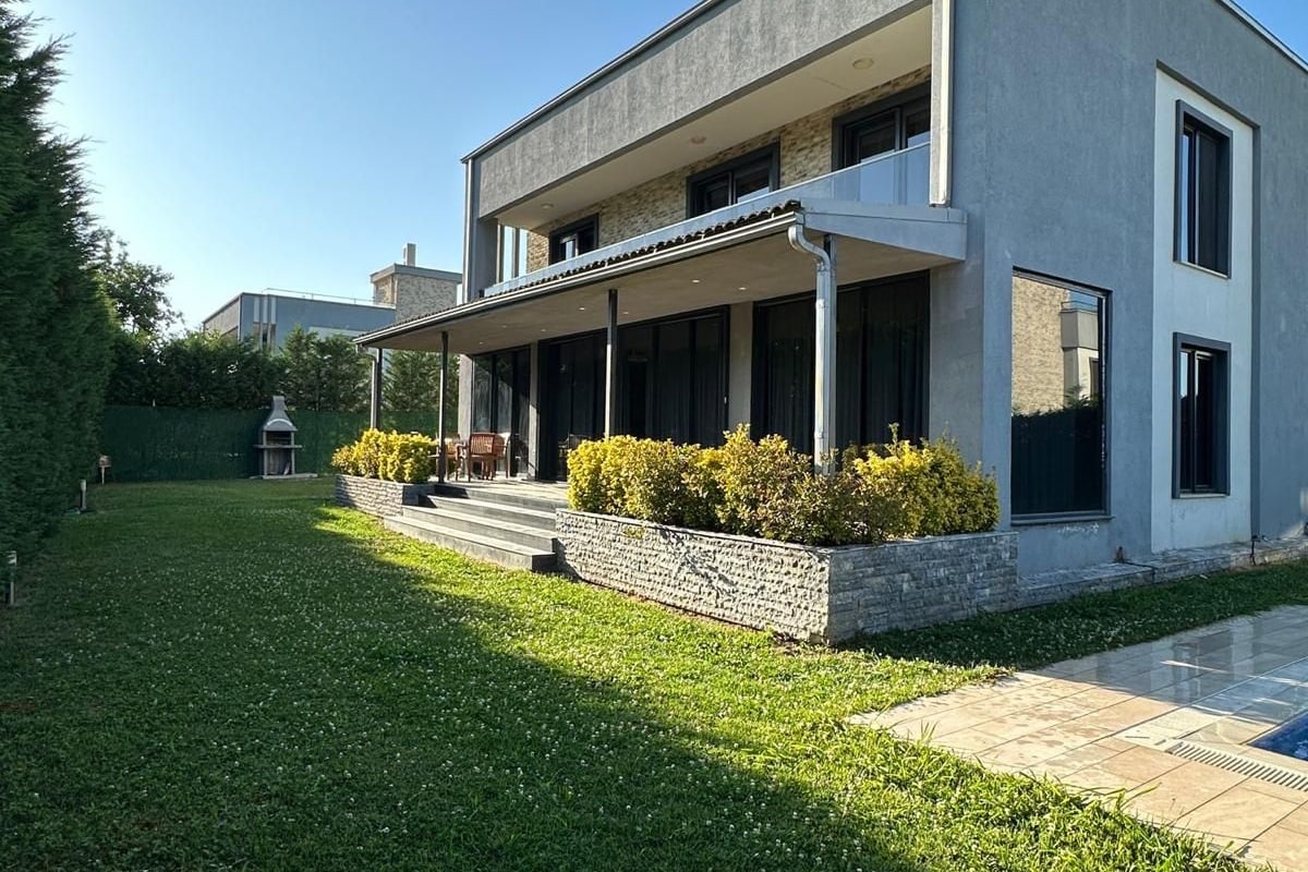 Una casa moderna de dos pisos con un porche cubierto, un césped cuidado y un muro de contención de piedra.