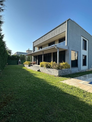 Una casa moderna de dos pisos con un porche cubierto, un césped cuidado y un muro de contención de piedra.