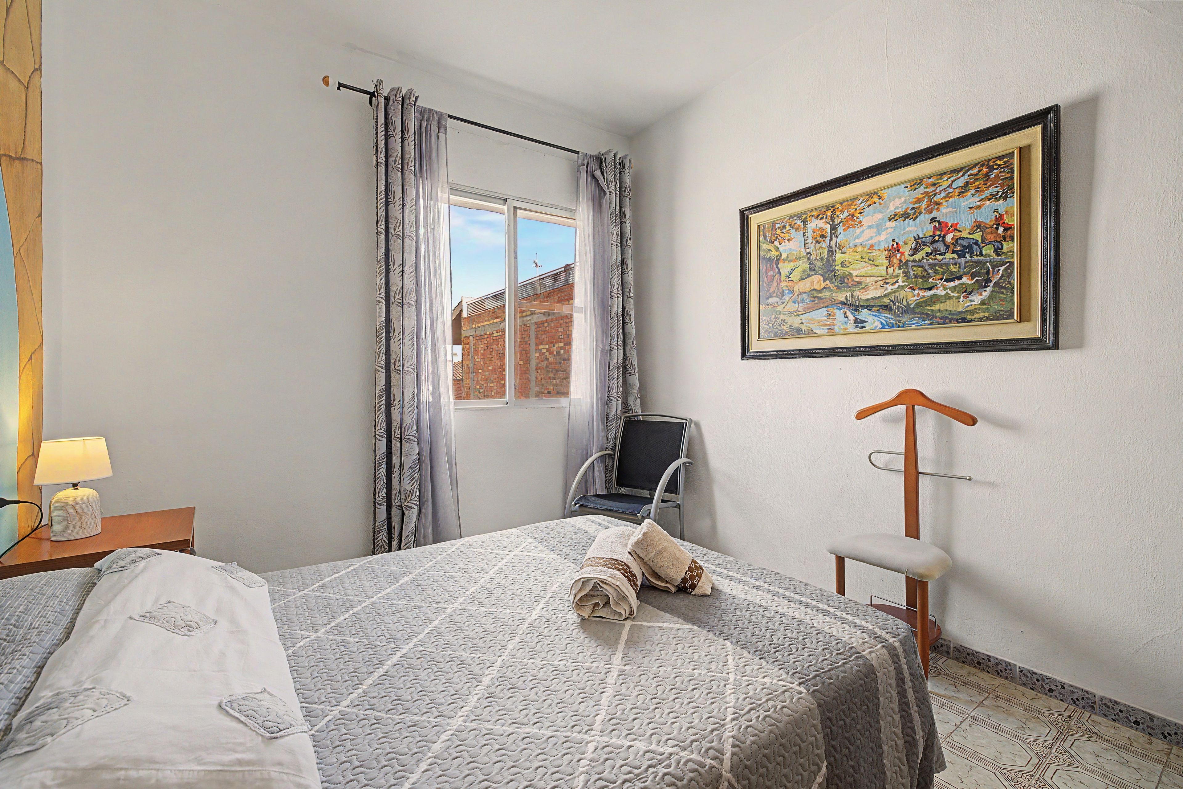 Une chambre d’hôtel avec un lit, une chaise, un tableau et une fenêtre avec des rideaux.