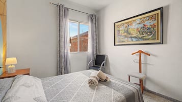 Une chambre d’hôtel avec un lit, une chaise, un tableau et une fenêtre avec des rideaux.