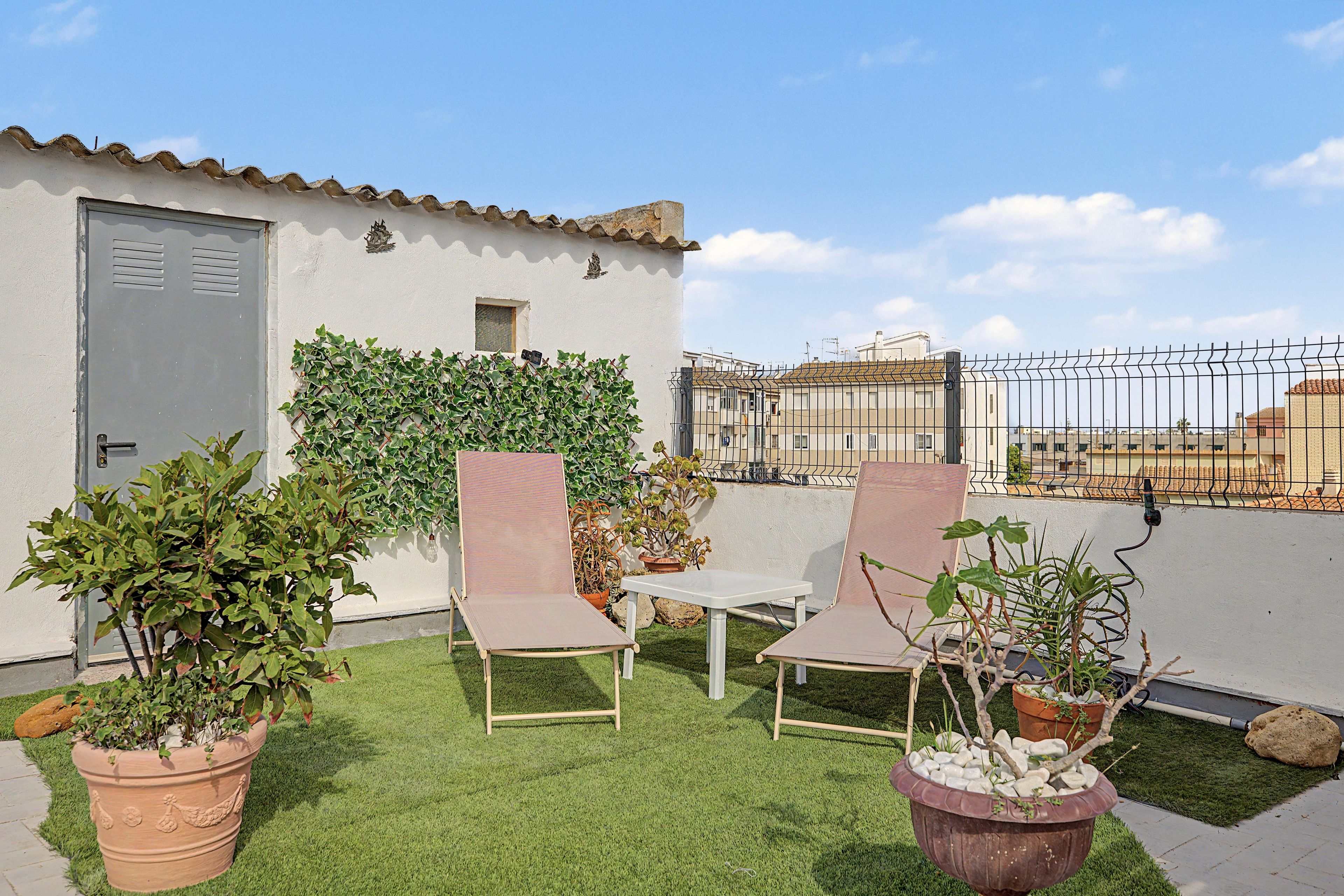 Una terraza en la azotea con dos sillones, una mesita y plantas en macetas.