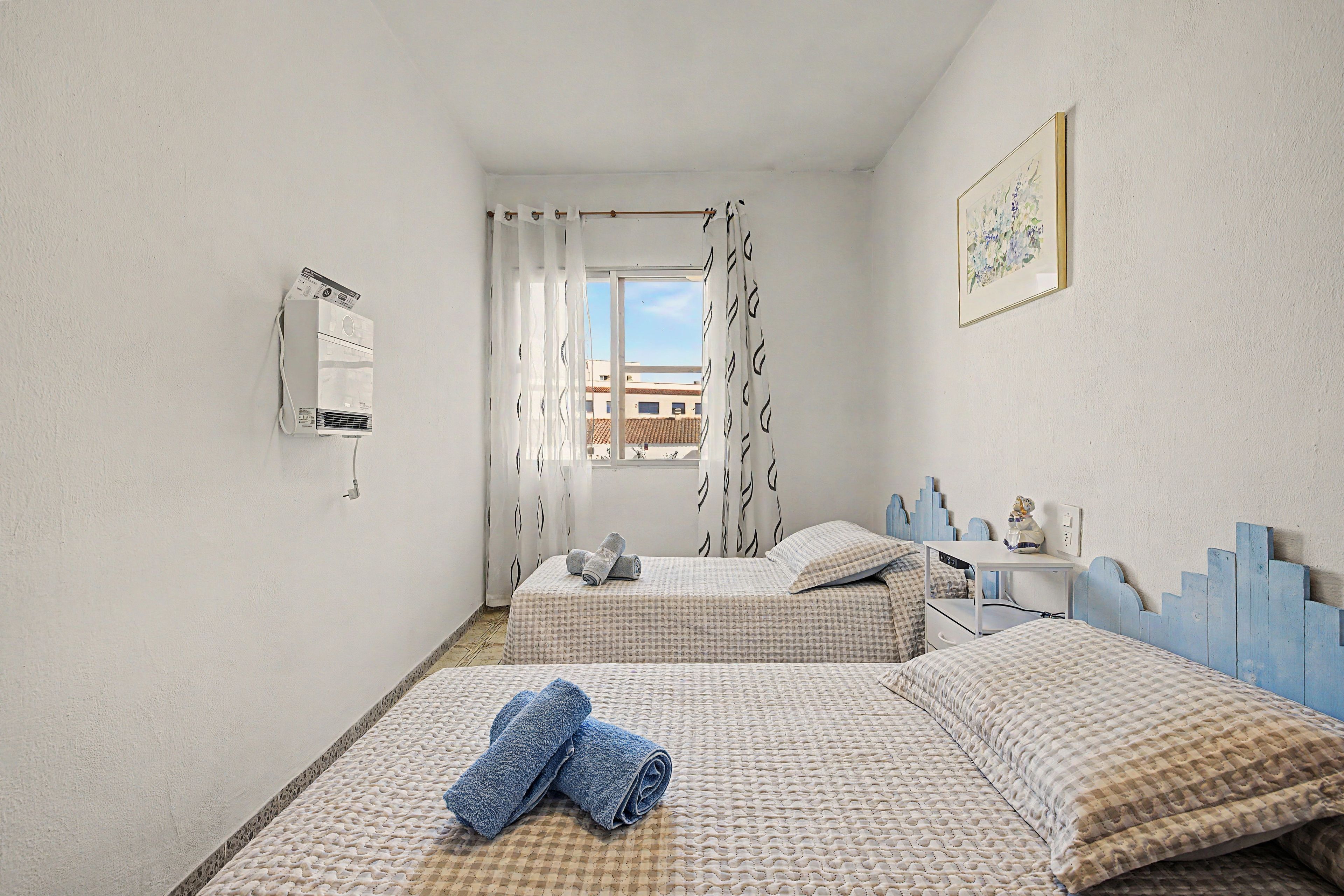 Un dormitorio con dos camas, una ventana con cortinas, un aire acondicionado de pared y un cuadro.