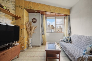 A living room with a television, a sofa, a decorative vase, and a view of the city through a window.