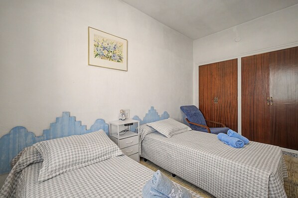 A bedroom with two beds, a nightstand, a chair, a wardrobe, and a painting on the wall.