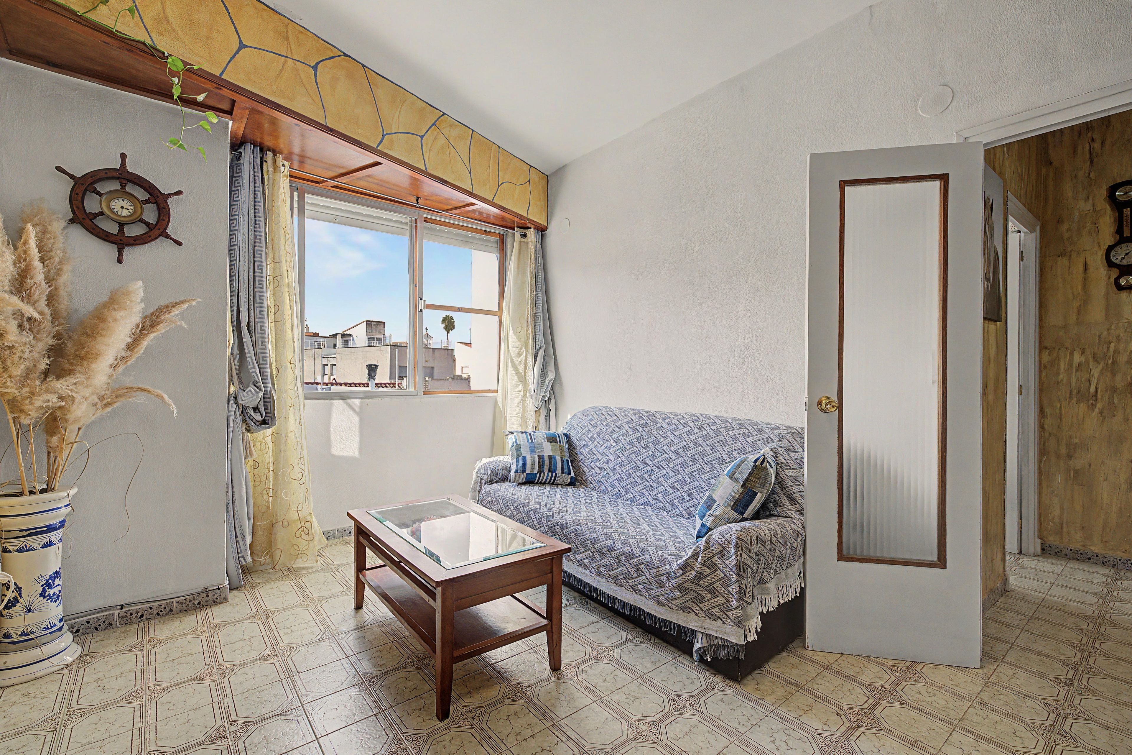 A room with a sofa, a small table, a potted plant, a window with curtains, and a door.