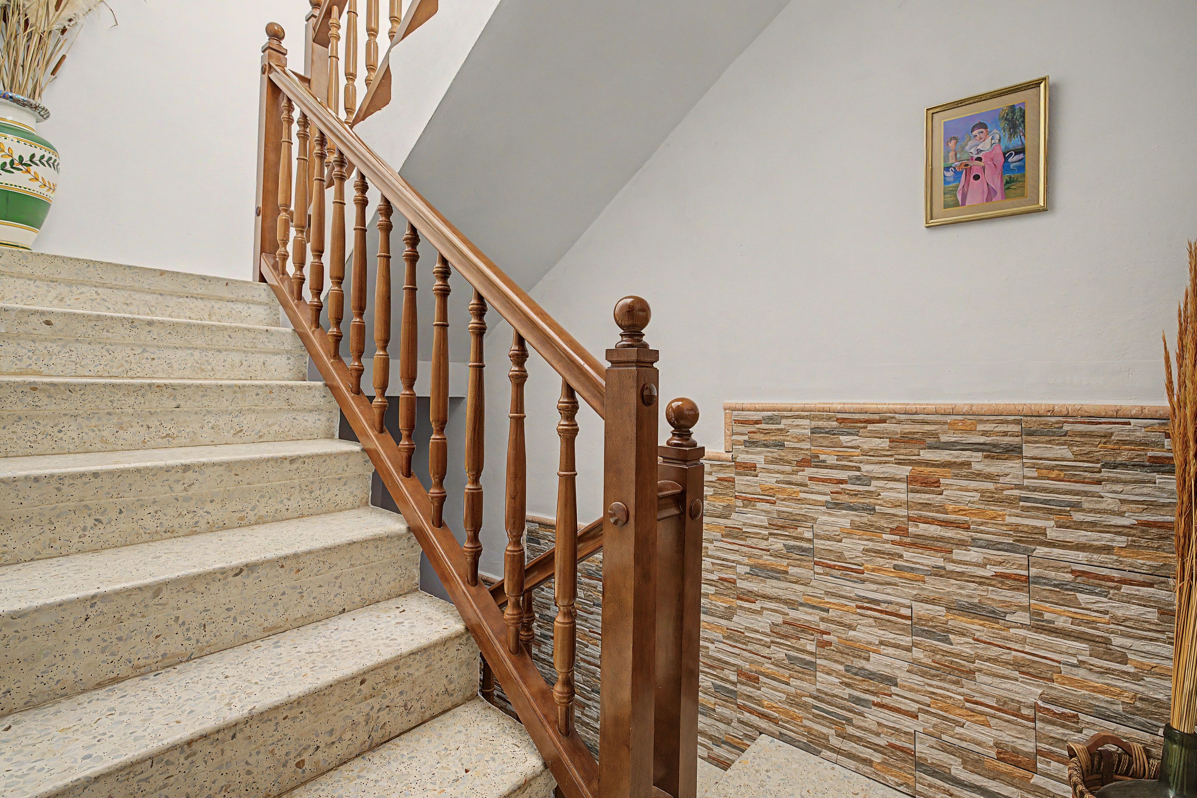 Una escalera con balaustres de madera y un muro de piedra.