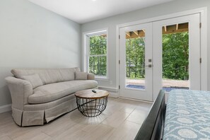 Ein Zimmer mit einem beigefarbenen Sofa, einem runden Couchtisch und einem Bett mit einem gemusterten Überwurf.