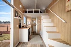 A modern kitchen with a central island, wooden walls, and a view of the outdoors.
