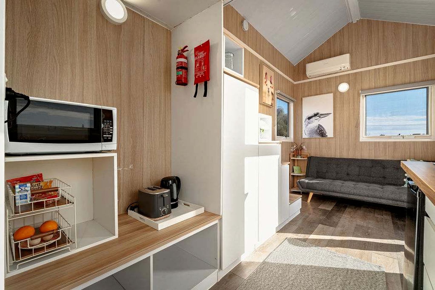 Eine kleine Küchenzeile mit Mikrowelle, Toaster und Kaffeemaschine, ein graues Sofa und ein Fenster mit Blick.