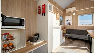Eine kleine Küchenzeile mit Mikrowelle, Toaster und Kaffeemaschine, ein graues Sofa und ein Fenster mit Blick.