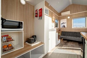 A compact kitchenette with a microwave, toaster, and coffee maker, a gray sofa, and a window with a view.