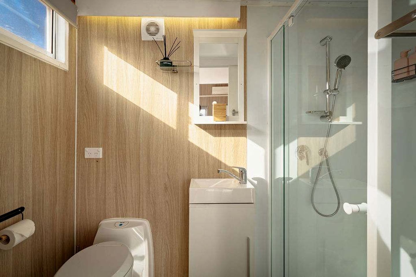 A modern bathroom with a wooden wall, a glass shower enclosure, a toilet, and a sink.