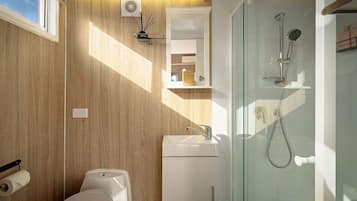 A modern bathroom with a wooden wall, a glass shower enclosure, a toilet, and a sink.