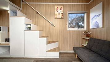 A modern interior with a staircase, a gray sofa, and a window with a view of trees.