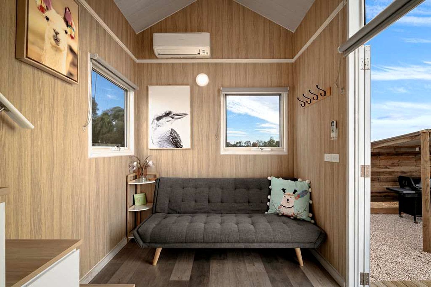 Una habitación acogedora con un sofá gris, una mesita con una planta y una ventana con vistas al cielo.