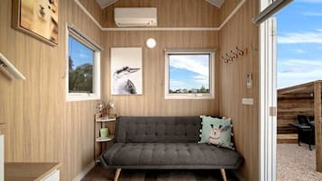 Una habitación acogedora con un sofá gris, una mesita con una planta y una ventana con vistas al cielo.