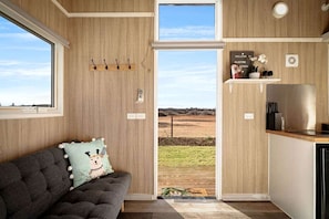 A cozy room with a sofa, a view of the outdoors, and a kitchen area.