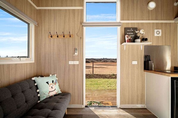 A cozy room with a sofa, a view of the outdoors, and a kitchen area.