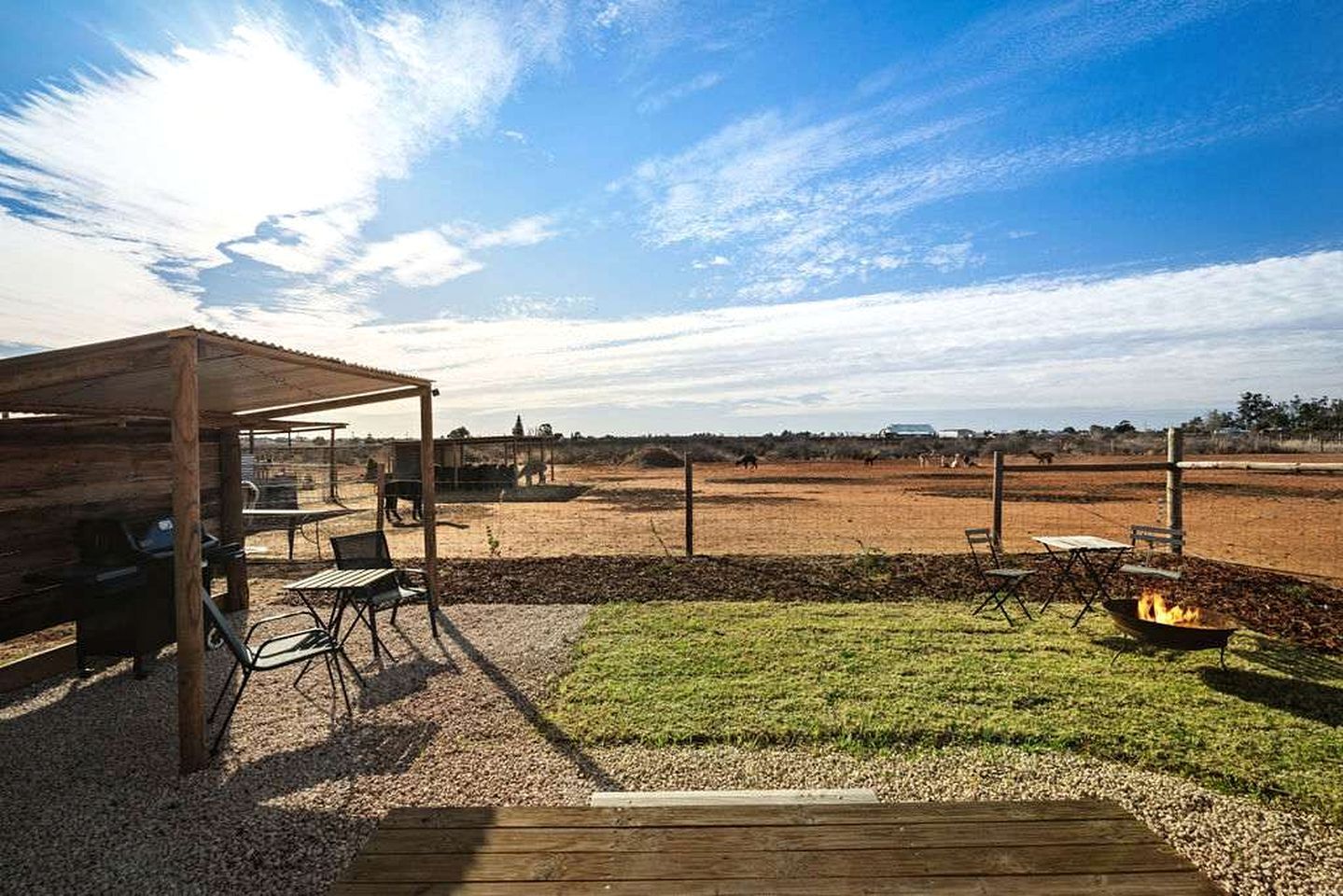 An outdoor patio area with a wooden pergola, seating, and a fire pit.