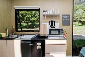 Une cuisine compacte équipée d’un évier, d’un four à micro-ondes et d’une machine à café. Une fenêtre offre une vue sur la verdure environnante.
