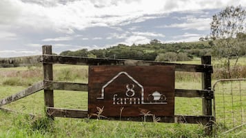 A wooden farm sign with a house and silo symbol, surrounded by a rustic fence and a grassy field.