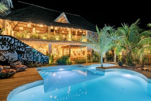 A pool area with a thatched-roof building, surrounded by tropical plants. - Oke Ani Boutique Hotel (PAJE)