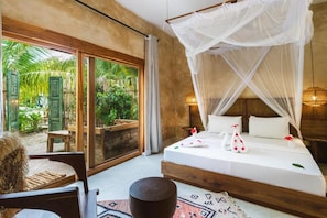 A bedroom with a bed, a nightstand, a bedside table, a chair, and a large window with a view of greenery. - Oke Ani Boutique Hotel (PAJE)