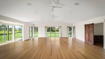 Quarto espaçoso com grandes janelas, piso de madeira e ventilador de teto.