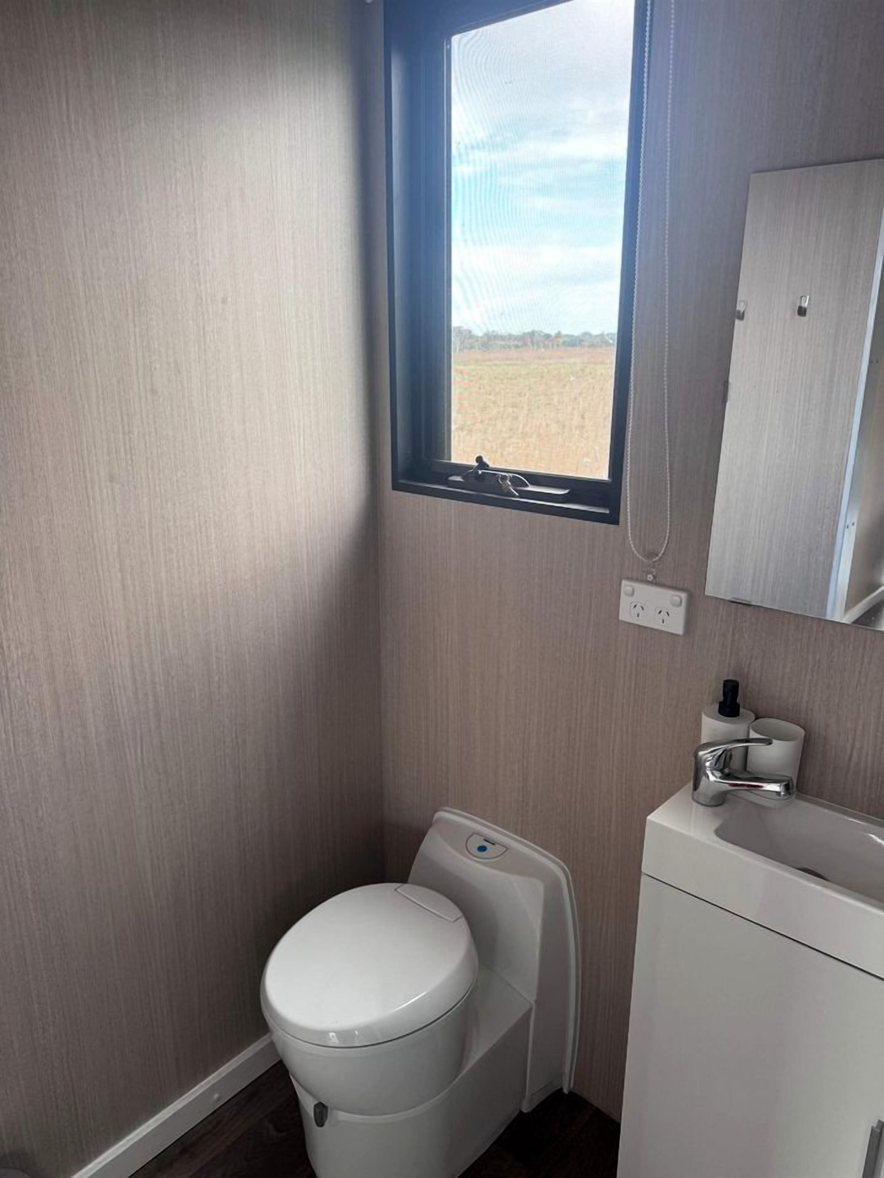 A compact bathroom with a toilet, sink, and a window providing a view of the outdoors.