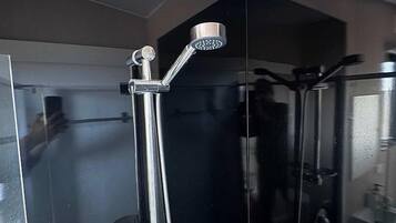A modern bathroom with a glass enclosure, a handheld showerhead, and a visible toilet.