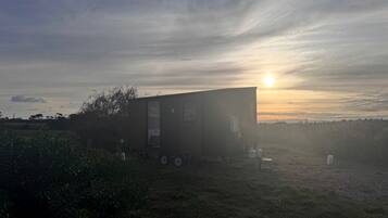 Une maison mobile de plain-pied, dotée d’un toit plat, située dans un champ verdoyant, avec un coucher de soleil en arrière-plan.