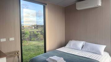 Ein Hotelzimmer mit großem Fenster, einem Bett mit weißer Bettwäsche und einer Klimaanlage an der Wand.