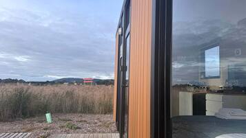 Un bâtiment moderne doté de grandes fenêtres, d’une terrasse en bois et offrant une vue sur un champ et des collines lointaines.