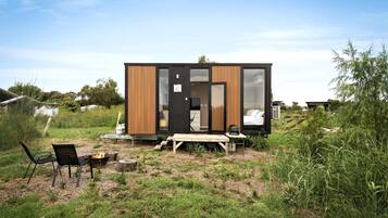 A modern, compact cabin with a wooden exterior, a small deck, and a fire pit.