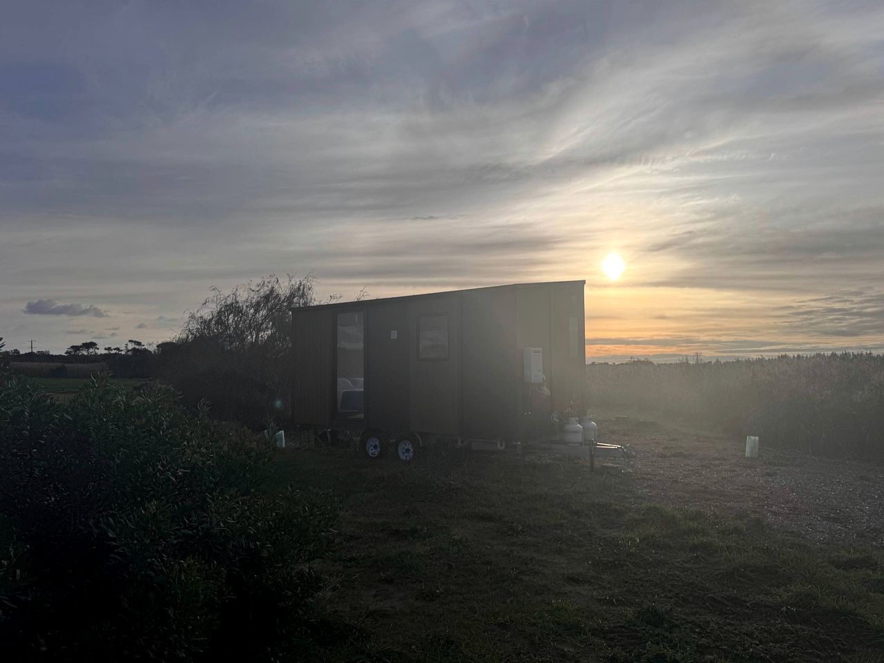 A single-story mobile home with a flat roof, positioned in a grassy field with a sunset in the background.