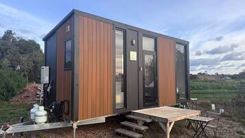 Une cabane moderne et compacte, dotée d’une façade en bois, de grandes portes vitrées et d’une terrasse en bois avec des sièges d’extérieur.