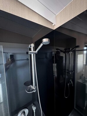 A modern bathroom with a glass enclosure, a handheld showerhead, and a visible toilet.