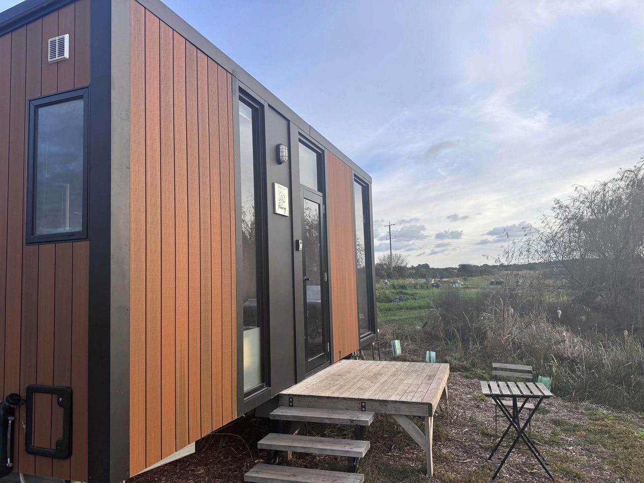 A modern, compact cabin with a wooden exterior, a sliding door, and a small outdoor seating area with a table and benches.