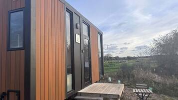 A modern, compact cabin with a wooden exterior, a sliding door, and a small outdoor seating area with a table and benches.