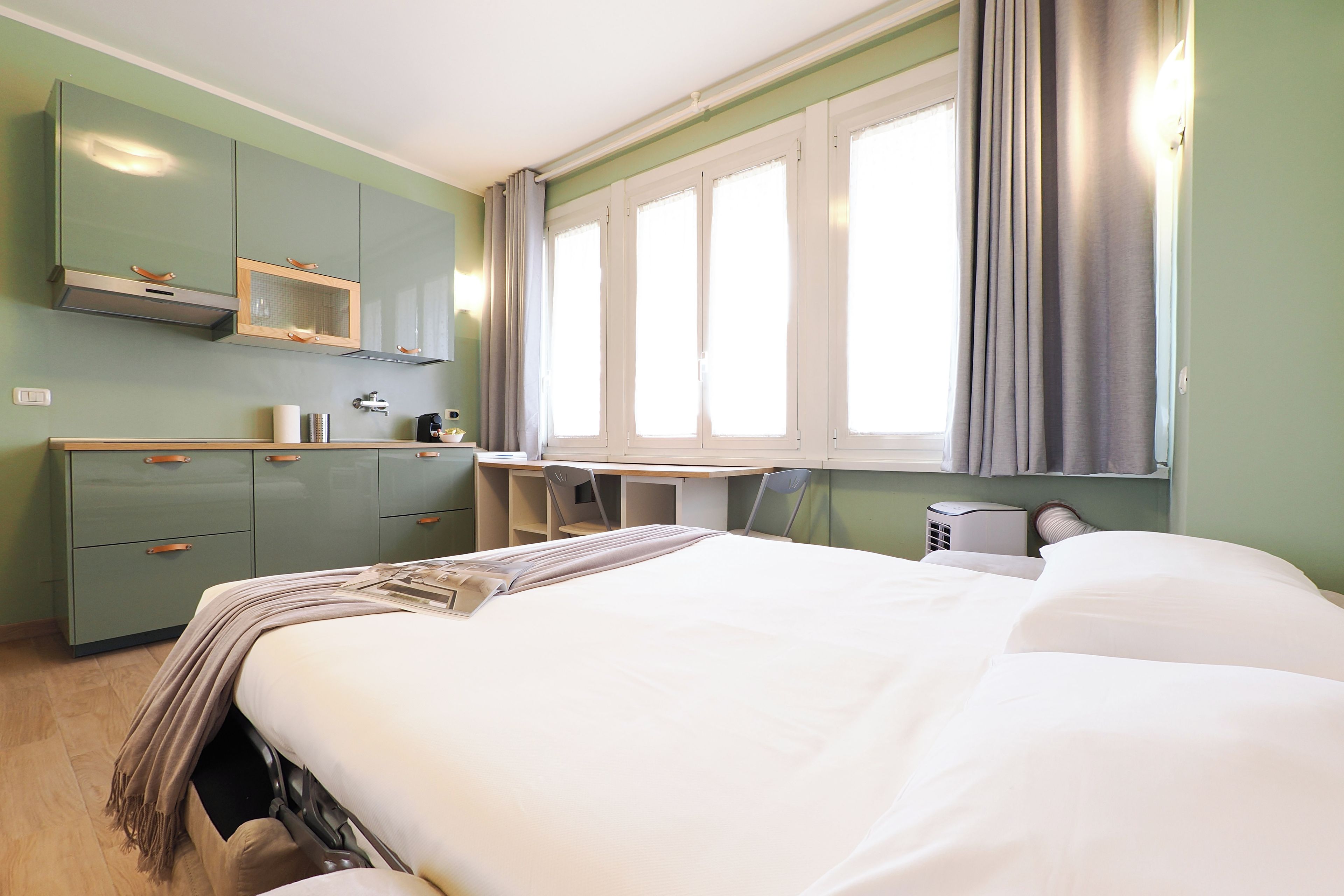 A room with a bed, a desk, and a kitchenette.