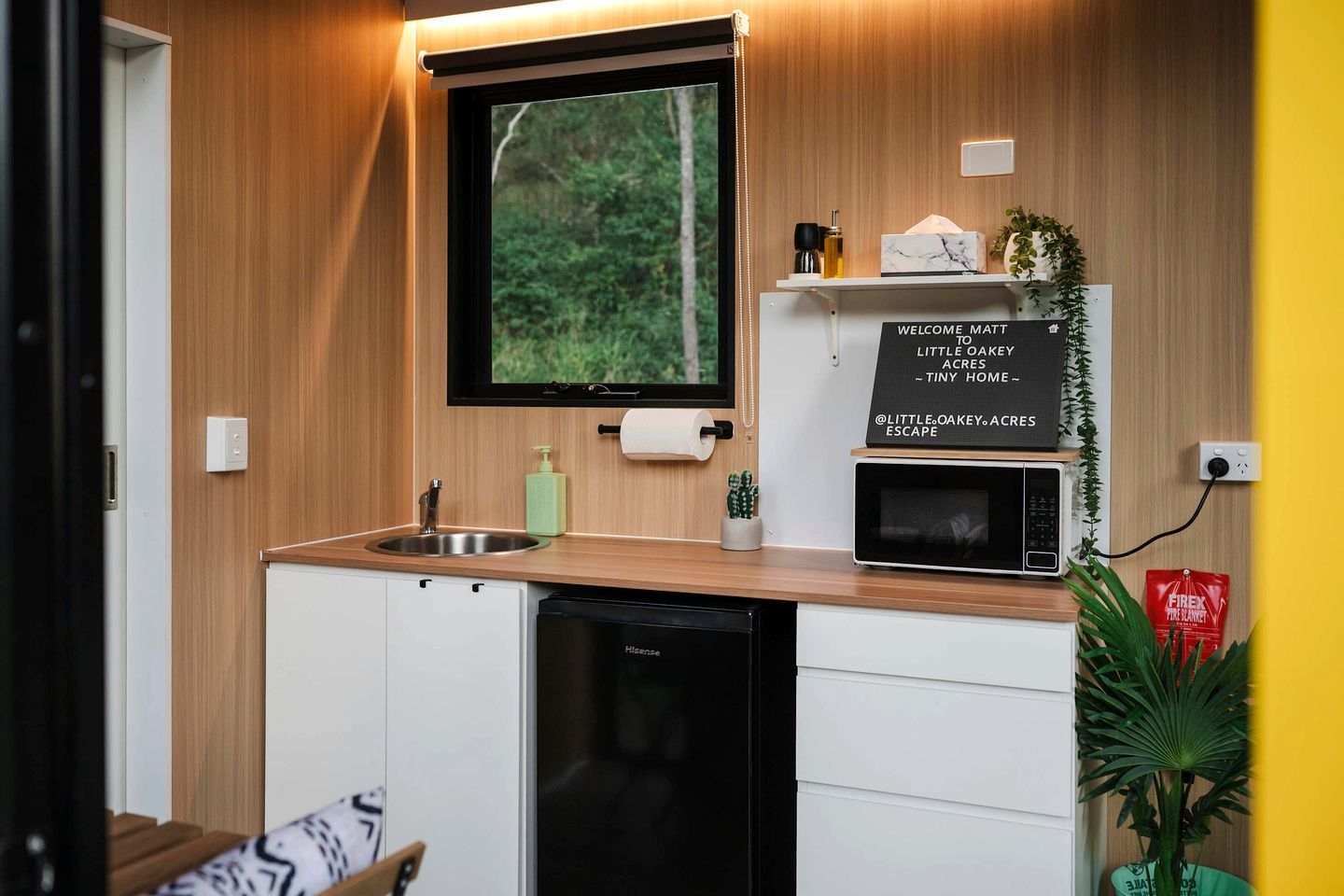 Une cuisine compacte équipée d’un four à micro-ondes encastré, d’un évier et d’un petit placard.