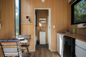 A compact kitchen with a sink, a dishwasher, and a window overlooking a forest.