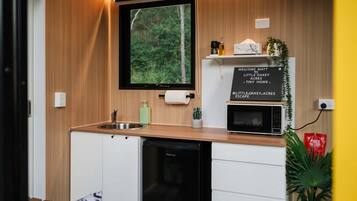 Una cocina compacta con microondas integrado, un lavamanos y un mueble pequeño.
