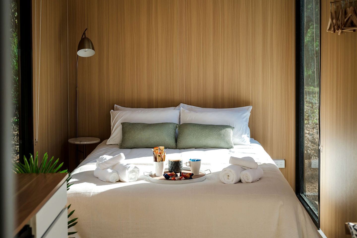 A neatly made bed with pillows, a bedside lamp, and a tray with towels and a mug.