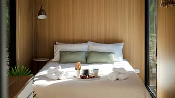 A neatly made bed with pillows, a bedside lamp, and a tray with towels and a mug.