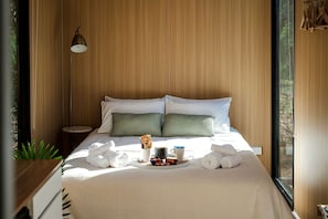 Un lit bien fait, avec des oreillers, une lampe de chevet et un plateau contenant des serviettes et une tasse.